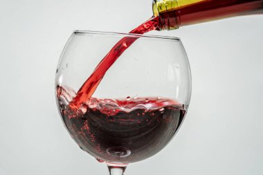 Kırmızı üzüm şarabı şişenin boynundan beyaz arka planda bir şarap bardağına dökülüyor. Tatma oturumu