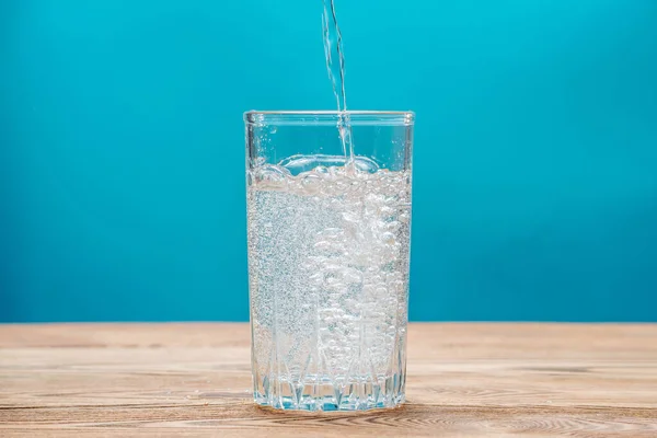 Pure fresh carbonated water with bubbles in a glass on a blue background