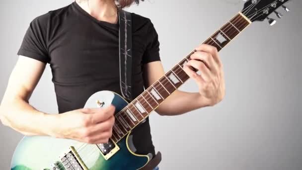 若い男がエレキギターを弾いて長い髪を振っている。ロックとロールの感情的なパフォーマンス — ストック動画