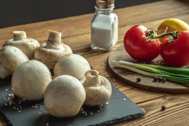 Tahta bir masada mantarlar, sebzeler ve baharatlar. Lezzetli yemekler pişirmek için gerekli malzemeler..