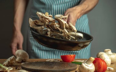 Aşçı tavaya taze doğranmış mantar atıyor. Yemek pişirme süreci kavramı.