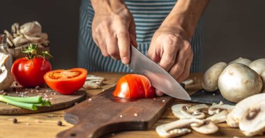Mavi önlüklü şef yemek hazırlamak için taze domatesleri bıçakla kesiyor. Yemek pişirme süreci kavramı