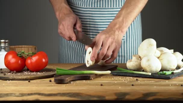 파란 앞치마를 입은 한 남자 요리사가 칼로 버섯을 자르고 있습니다. 맛있는 요리를 만드는 과정의 개념 — 비디오