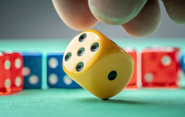 The hand is throwing yellow dice on the green table. The concept of a casino and a lucky chance to win