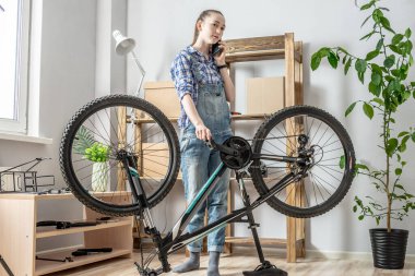 Genç bir kadın bisiklet tamir ediyor ve cep telefonu kullanıyor. Motorun yeni sezon için bakım ve hazırlık kavramı