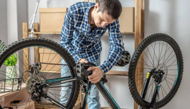 Genç adam atölyede bir dağ bisikletini tamir ediyor. Yeni sezon için hazırlık kavramı, onarım ve bakım