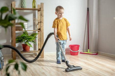 Küçük bir çocuk anne ve babasına ev işlerinde yardım ediyor, yerleri süpürgeyle temizliyor.