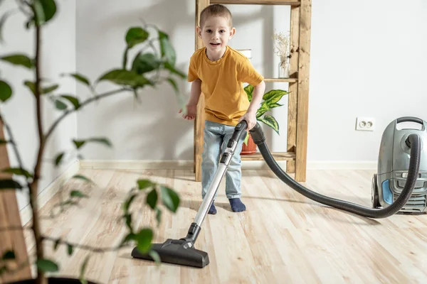 A little child helps his parents in housework, cleaning the floor using a vacuum cleaner
