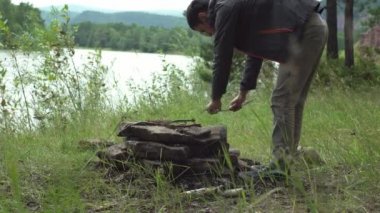 Nehir kenarındaki ormanda yürüyüşçü ateş yakmak için kuru dallar koyuyor. Yürüyüş kavramı, vahşi doğada zaman geçirme.