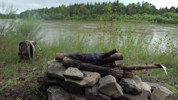 Річка з швидкою течією, лісом, багаттям і рюкзаком для туристів. Концепція тихого і мирного проведення часу в природі — стокове відео