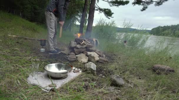 El hombre en el bosque junto al río está encendiendo un fuego. Concepto de habilidades de supervivencia en la naturaleza, haciendo una fogata para cocinar — Vídeos de Stock