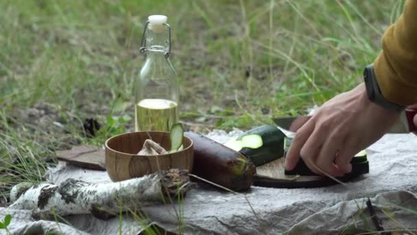 Man in the forest by the fire is cutting vegetables for cooking. Concept of survival skills in the wild, hiking — Stock Video