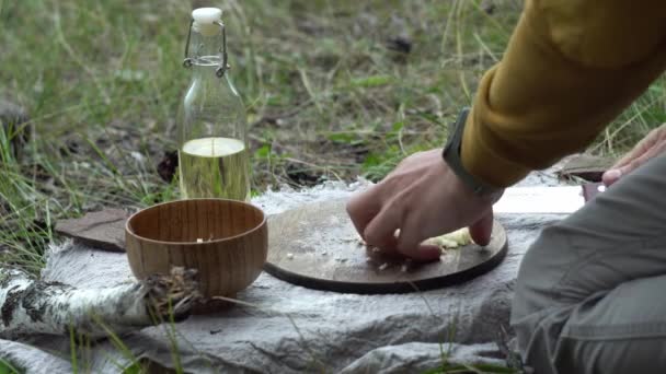 El hombre en el bosque junto al fuego está cortando verduras para cocinar. Concepto de habilidades de supervivencia en la naturaleza, senderismo — Vídeos de Stock