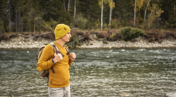 男性の旅行者は 秋の森を背景に海岸沿いに巨大な石を持つ速い山の川に沿って歩いています ハイキングと旅の概念 — ストック写真