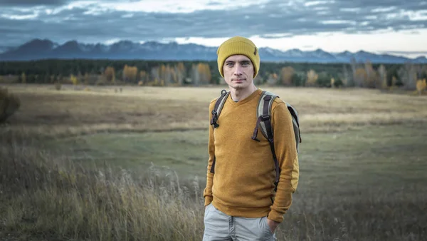 秋の黄金の森と山々を背景に 黄色の帽子と自然界のセーターを着た旅行者 ハイキング 秋の気分の概念 — ストック写真