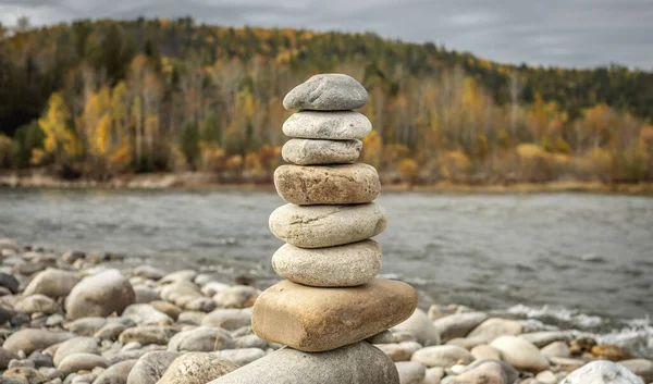 Pile of stones built in cairn on the background of river. Concept of calmness and detachment with nature