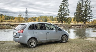 Araba hızlı bir nehrin kıyısında, sarı yeşil bir sonbahar ormanının yanında park halinde. Seyahat kavramı, güzel doğa ve sonbahar havası.