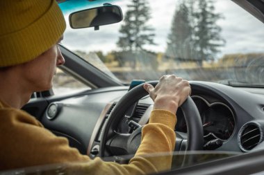 Sarı şapkalı ve kazaklı bir adam nehir boyunca ve güzel sonbahar ormanlarında araba sürüyor. Doğa kavramı, seyahat ve sonbahar havası