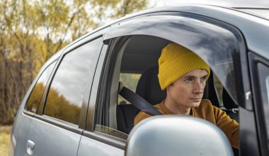 Sarı şapkalı ve kazaklı bir adam sonbahar orman yolunda araba sürüyor. Doğa kavramı, seyahat ve sonbahar havası.