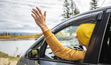 Sarı şapkalı ve kazaklı bir adam nehir boyunca ve güzel sonbahar ormanlarında araba sürüyor. Doğa kavramı, seyahat ve sonbahar havası