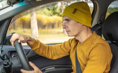 Sarı şapkalı ve kazaklı bir adam sonbahar orman yolunda araba sürüyor. Doğa kavramı, seyahat ve sonbahar havası.