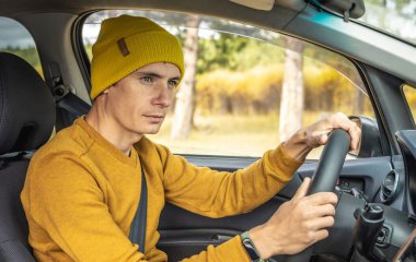 Sarı şapkalı ve kazaklı bir adam sonbahar orman yolunda araba sürüyor. Doğa kavramı, seyahat ve sonbahar havası.