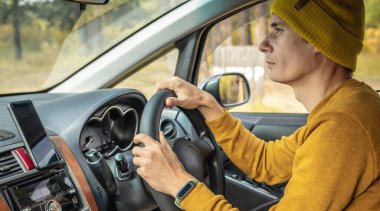 Sarı şapkalı ve kazaklı bir adam sonbahar orman yolunda araba sürüyor. Doğa kavramı, seyahat ve sonbahar havası.