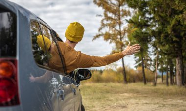 Adam nehir ve orman boyunca araba sürüyor, arabanın camından dışarı eğiliyor ve elini uzatıyor, sessizliğin, güneş ışığının ve güzel sonbahar doğasının tadını çıkarıyor. Sonbahar havası.