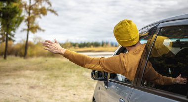 Adam nehir ve orman boyunca araba sürüyor, arabanın camından dışarı eğiliyor ve elini uzatıyor, sessizliğin, güneş ışığının ve güzel sonbahar doğasının tadını çıkarıyor. Sonbahar havası.