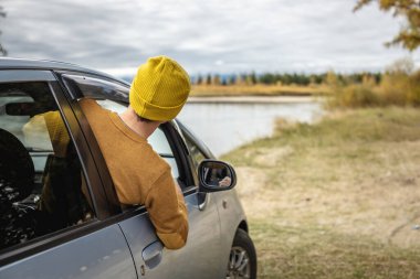 Adam nehir ve orman boyunca araba sürüyor, arabanın camından sarkmış, sessizliğin, güneş ışığının ve güzel sonbahar doğasının tadını çıkarıyor. Sonbahar havası.