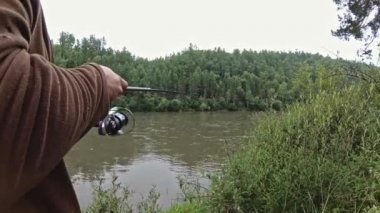 Nehir kıyısında elinde olta ve balık tutan bir adam var.