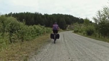 Bisikletçi yürüyüşçü şehir dışındaki ağaçların arka planına karşı yolda bisiklet sürüyor. Arkadan bak.