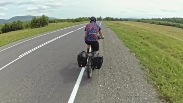 Ciclista excursionista monta una bicicleta en la carretera contra el fondo de los árboles fuera de la ciudad. Vista desde atrás — Vídeos de Stock