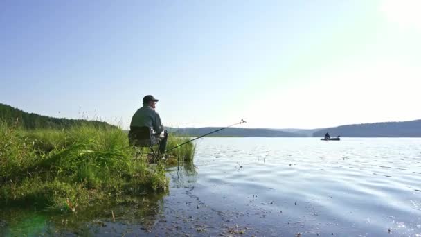 Muž stojí na břehu řeky s rybářským prutem v rukou a chytá ryby — Stock video