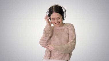 Kulaklıklı, gülümseyen bir kadın gradyan arka planda müzik eşliğinde yürüyor ve dans ediyor..