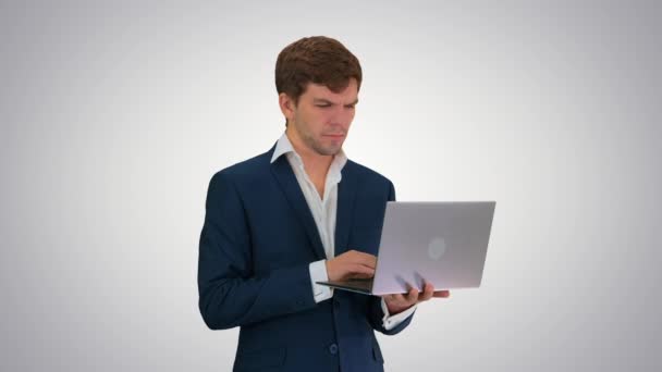 Concentrado joven empresario que trabaja en el ordenador portátil, mientras que de pie en el fondo gradiente. — Vídeos de Stock