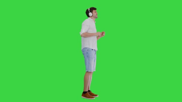 Casual jovem em fones de ouvido ouvir música e apreciá-lo em uma tela verde, Chroma Key. — Vídeo de Stock