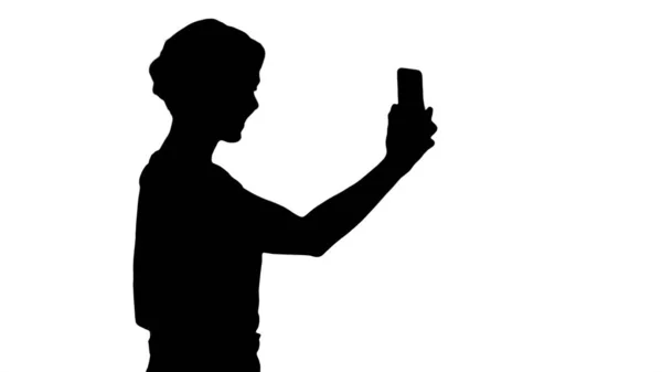 Silhouette Schöne junge Frau geht und hält ein Smartphone in der Hand — Stockfoto