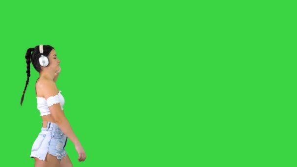 Femme latine aux cheveux noirs profitant de la musique dans les écouteurs et marchant sur un écran vert, Chroma Key. — Video