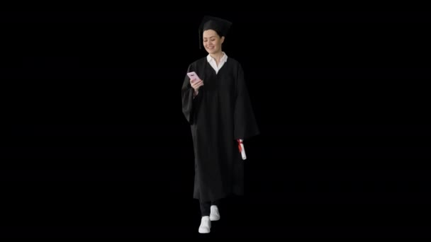 Mujer sonriente graduada en mensajes de texto de mortero en su teléfono mientras camina, Alpha Channel — Vídeo de stock