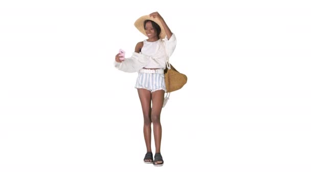Hasır şapkalı gülümseyen Afrikalı Amerikalı kadın beyaz arka planda yürürken selfie çekiyor.. — Stok video