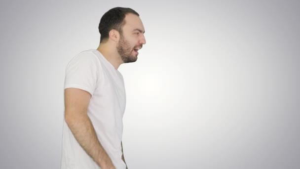 Sleepy male in white t-shirt yawning and rubbing eyes while walking on gradient background. — Stock Video