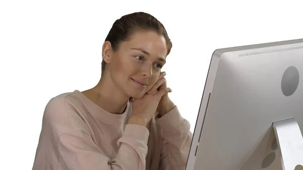 Chica rubia con suéter rosa mirando el monitor de la computadora viendo vídeo sobre fondo blanco. — Foto de Stock