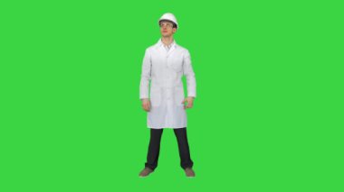 Beyaz cüppeli, güvenlik kasklı ve gözlüklü bilim adamı yeşil ekranda gözleriyle komik hareketler yapıyor, Chroma Key..