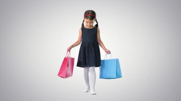 Vacker liten flicka i svart klänning promenader med shoppingväskor på lutning bakgrund. — Stockvideo