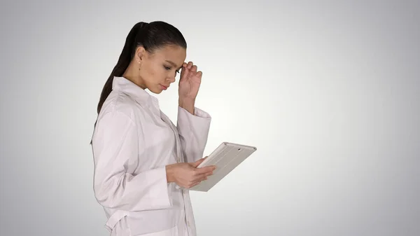 Женщина врач с помощью планшетного ПК и ходить на градиентном фоне. — стоковое фото
