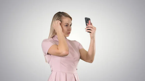 Blondynka preening przed smartfonem na gradient bac — Zdjęcie stockowe