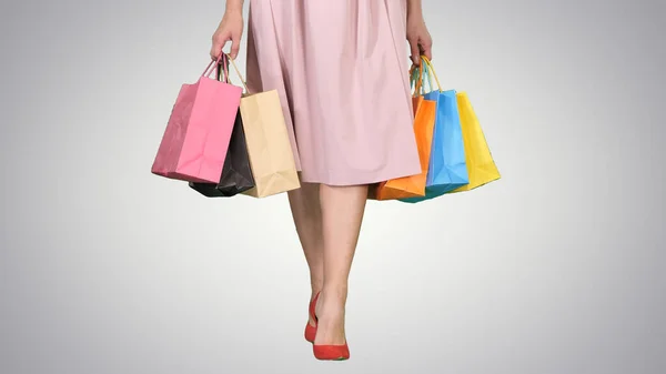 Young woman legs carrying colorful shopping bags on gradient bac — Stock Photo, Image