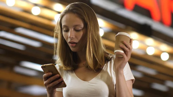 Piękna kobieta stojąca z filiżanką kawy, smsująca przez telefon. — Zdjęcie stockowe