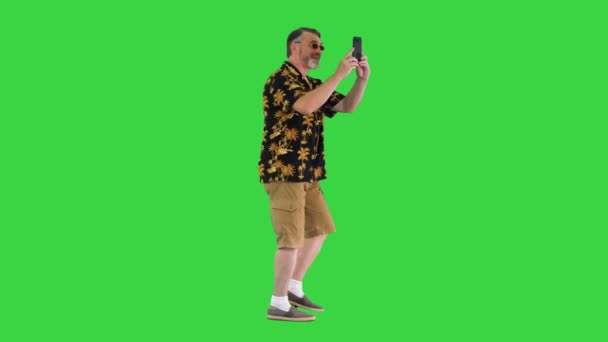 緑の画面に彼の携帯電話で写真を撮る幸せなシニアひげを生やした観光客の男、クロマキー. — ストック動画